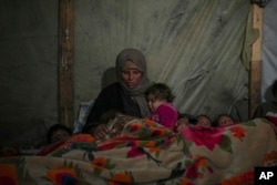 Reda Abu Zarada wraps herself and her grandchildren in blankets as they prepare to sleep in their tent at a camp in Khan Younis, Gaza Strip, Dec. 19, 2024.