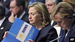 U.S. Secretary of State Hillary Rodham Clinton, center, reads a document as she sits next to German Chancellor Angela Merkel at the start of the OSCE Summit at the Palace of Independence in Astana, Kazakhstan, 01 Dec 2010