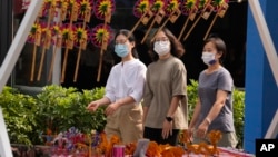 在中国北京街头戴着口罩的妇女经过一个摆放风车玩具的摊位（2022年9月13日）。