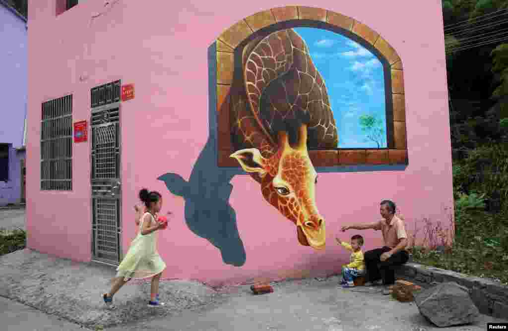 Tourists play in front of a 3D painting on the wall of a house in Luoyuan village, Jinhua, Zhejiang province, Aug. 26, 2015.