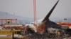 FILE - People stand as the wreckage of an aircraft lying on the ground after it went off the runway and crashed at Muan International Airport is pictured, in Muan, South Korea, Dec. 30, 2024. 