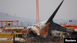 FILE - People stand as the wreckage of an aircraft lying on the ground after it went off the runway and crashed at Muan International Airport is pictured, in Muan, South Korea, Dec. 30, 2024. 