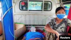 FILE - A relative sits with a COVID-19 patient being taken to hospital in the town of Kale, Sagaing region, Myanmar, July 6, 2021.