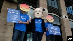 FILE - A protester wearing a mask with the face of Facebook founder Mark Zuckerberg is flanked by two fellow activists wearing angry face emoji masks, during a protest against Facebook policies, in London, Britain, April 26, 2018.