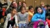 FILE -- Pittsburgh Mayor Bill Peduto, left rear, sits on the floor with a group of students from Oakland's Falk School during the first-day-of-issue dedication of the Mister Rogers Forever Stamp in WQED's Fred Rogers Studio in Pittsburgh, March 23, 2018.