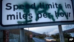 A sign on the border between Northern Ireland and the Republic of Ireland, spray painted with the initials of the Irish Republican Army, alerts drivers to the change in miles per hour for speed limit postings, Dec. 17, 2019, in Newry, Northern Ir