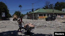 Una mujer empuja una carretilla llena de bolsas de pan cerca de un vehículo blindado de transporte de personal de la policía de Kenia y un vehículo blindado de la policía haitiana, en Puerto Príncipe, Haití, el 9 de septiembre de 2024.