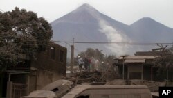 Rescue workers walk on rooftops in Escuintla, Guatemala, June 4, 2018, blanketed with heavy ash spewed by the Volcan de Fuego, or "Volcano of Fire," pictured in the background, left center. 