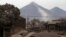 Rescue workers walk on rooftops in Escuintla, Guatemala, June 4, 2018, blanketed with heavy ash spewed by the Volcan de Fuego, or "Volcano of Fire," pictured in the background, left center. 