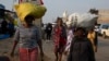 FILE - Women carry sacks on their heads down a busy street in the Diepsloot Township, north of Johannesburg, Thursday, Aug. 26, 2021. 