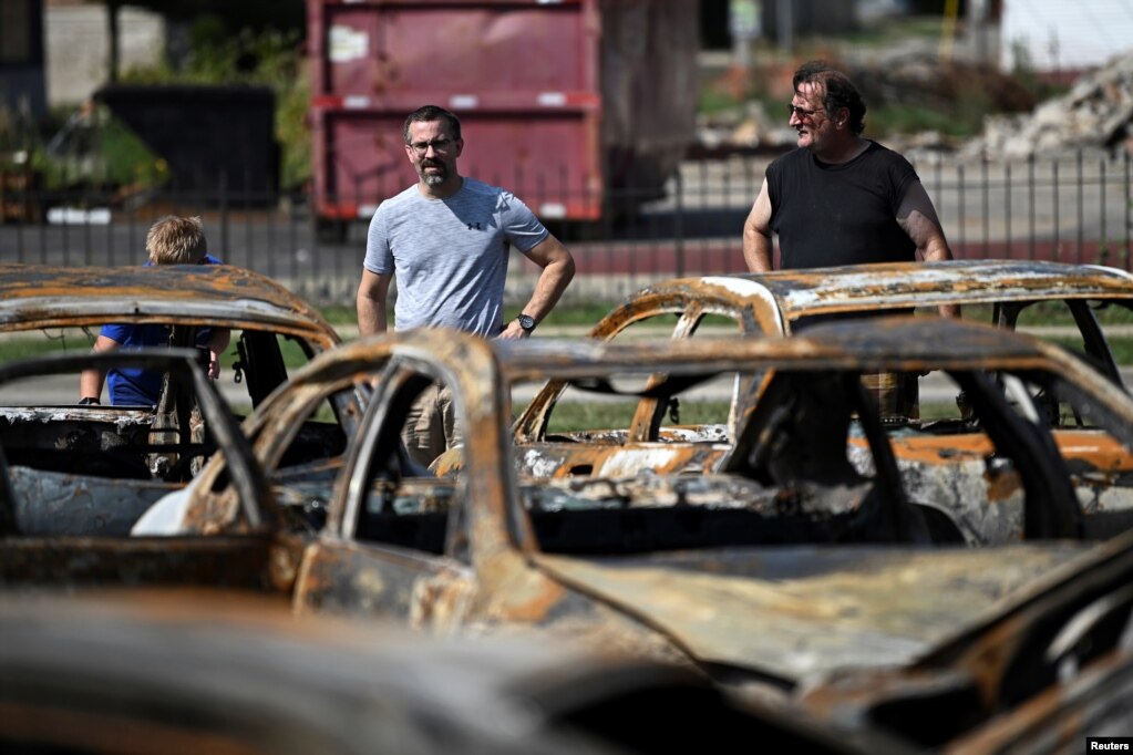 People stand in front of the damage at Car Source, a used car lot, after protests following the police shooting of Jacob Blake, a Black man, in Kenosha, Wisconsin, Aug. 27, 2020.