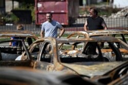People stand in front of the damage at Car Source, a used car lot, after protests following the police shooting of Jacob Blake, a Black man, in Kenosha, Wisconsin, Aug. 27, 2020.