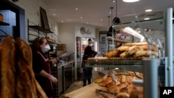 Bakers sell bread in a Boulogne Billancourt bakery, outside Paris, Tuesday, March 24, 2020. French President Emmanuel Macron urged employees to keep working in supermarkets, production sites and other businesses that need to keep running amid…