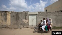 A family rides past the locked house of Rimsha Masih, a Pakistani Christian girl accused of blasphemy, on the outskirts of Islamabad, August 23, 2012.