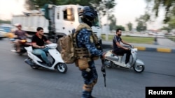 Men ride motorbikes past a member of Iraqi federal police in a street in Baghdad, Iraq October 7, 2019. 