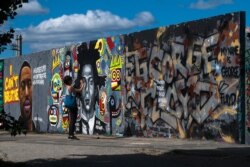 A woman takes a photo of a graffiti with the name of George Floyd, which is painted on a wall in the public park Mauerpark in Berlin, Germany, Saturday, May 30, 2020.
