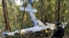 En esta foto proporcionada por la Oficina de Prensa de las Fuerzas Armadas de Colombia, un soldado permanece frente a los restos de una avioneta Cessna C206 el jueves 18 de mayo de 2023. La aeronave se estrelló en la selva de Solano, Colombia. 