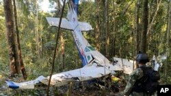 En esta foto proporcionada por la Oficina de Prensa de las Fuerzas Armadas de Colombia, un soldado permanece frente a los restos de una avioneta Cessna C206 el jueves 18 de mayo de 2023. La aeronave se estrelló en la selva de Solano, Colombia. 