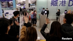 FILE - Members of a family who are emigrating to the United Kingdom wave good-bye to their friends, who are seeing them off before their departure, at Hong Kong International Airport in Hong Kong, Dec. 17, 2020. 