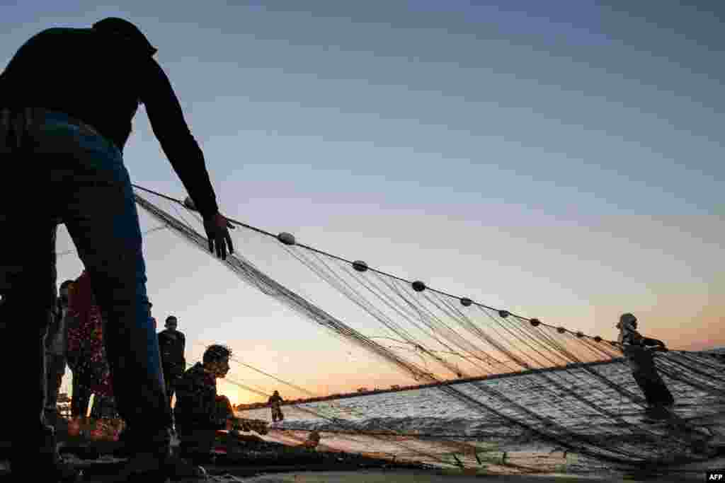 Palestinian fishermen retrieve their fishing nets back from the Mediterranean sea water at sunset in Gaza City.