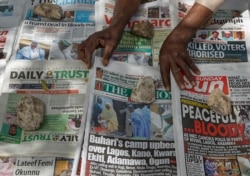 FILE - A newspaper vendor uses rocks to stop the day's front pages from blowing in the wind in Kano, northern Nigeria, Feb. 24, 2019.