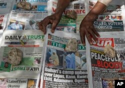 FILE - A newspaper vendor uses rocks to stop the day's front pages from blowing in the wind in Kano, northern Nigeria, Feb. 24, 2019.