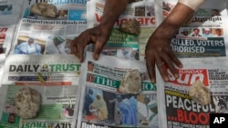 FILE - A newspaper vendor uses rocks to stop the day's front pages from blowing in the wind in Kano, northern Nigeria, Feb. 24, 2019.
