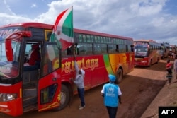 An adviser on repatriation hangs a Burundian flag on the lead bus transporting refugees arriving at the Gisuru border in Ruyigi, Burundi, Oct. 3, 2019.