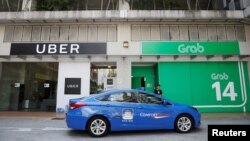 Sebuah taksi melewati kantor Uber dan Grab di Singapura, 26 Maret 2018.