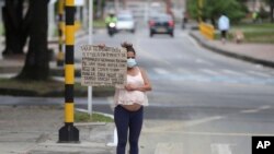 La migrante venezolana Verónica Hernández, de 20 años, embarazada de ocho meses, sostiene un cartel con un mensaje escrito a mano pidiendo comida o dinero, en un paso de peatones en Bogotá, Colombia, el martes 9 de febrero de 2021.