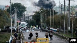 Seorang perempuan menutup telinga menyusul ledakan di sebuah jembatan di atas Sungai Oskil. Asap membubung dari garis depan pertempuran pasukan Ukraina dan Rusia di Kota Kupiansk, Kharkiv, Sabtu, 24 September 2022. (Foto: Yasuyoshi Chiba/AFP)