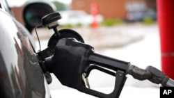 FILE - The handle from a gasoline pump hangs from the filler neck of a motorist's vehicle at a Shell station, July 31, 2021, in Englewood, Colo. Gas prices have fallen in recent months, easing the strain on Americans' budgets.