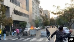 In this Sept. 20, 2022, photo taken by an individual not employed by the Associated Press and obtained outside Iran, protesters throw stones at police during a protest over the death of a young woman detained for violating the country's conservative dress code, in Tehran.