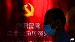 A man wearing a face mask walks by a propaganda poster welcoming the 20th party congress, along a street in Beijing, Sept. 20, 2022. 