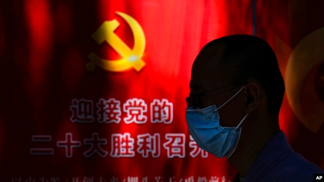 A man wearing a face mask walks by a propaganda poster welcoming the 20th party congress, along a street in Beijing, Sept. 20, 2022.