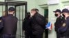 FILE - An opposition activists is escorted to a defendant's cage before a verdict hearing in his trial on charges of organizing riots and inciting social hatred, at a detention center in Gomel, Belarus, Dec. 14, 2021.