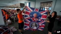 General manager Fan Aiping holds up flags with the Queen's image at the Shaoxing Chuangdong Tour Articles Co. factory in Shaoxing, in eastern China's Zhejiang province, Sept. 16, 2022.