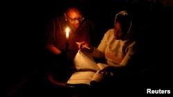 FILE - Thandiwe Sithole studies by a candle while her grandmother Phumzile Sithole looks on during one of frequent power outages from South African utility Eskom caused by its aging coal-fired plants, in Soweto, South Africa, March 9, 2022.