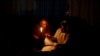 FILE - Thandiwe Sithole studies by a candle while her grandmother Phumzile Sithole looks on during one of frequent power outages from South African utility Eskom caused by its aging coal-fired plants, in Soweto, South Africa, March 9, 2022.