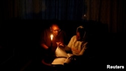 FILE - Thandiwe Sithole studies by a candle while her grandmother Phumzile Sithole looks on during one of frequent power outages from South African utility Eskom caused by its aging coal-fired plants, in Soweto, South Africa. Take 3.9.2022