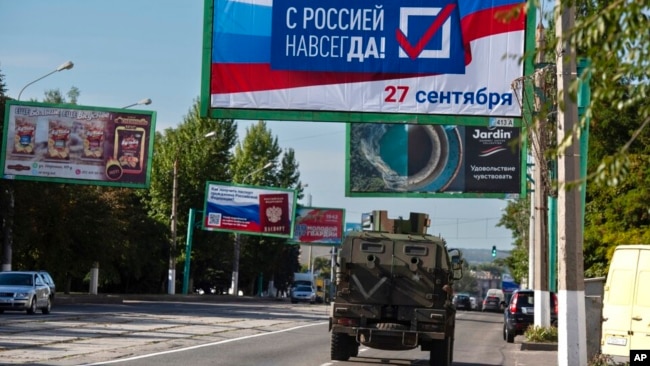 Një makinë ushtarake kalon nën një pankartë ku shkruhet "Me Rusinë përgjithmonë, 27 shtator", në prag të zhvillimit të referendumit në Luhansk, Ukraina lindore (22 shtator 2022)