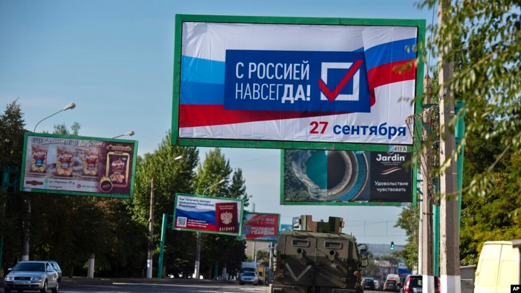 2022年9月22日俄罗斯支持的东乌克兰卢甘斯克人民共和军分离主义者操纵的公投举行之前，一辆军车驶过一条挂满宣传看板的街道。一块看板上写着“9月27日，永远同俄罗斯在一起”。 (photo:VOA)