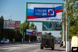 A military vehicle drives along a street with a billboard that reads: 'With Russia forever, September 27', prior to a referendum in Luhansk, Luhansk People's Republic controlled by Russia-backed separatists, eastern Ukraine, Sept. 22, 2022.