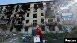 A member of an electoral commission walks past a destroyed building with a mobile ballot box and documents on the third day of a referendum on the joining of the self-proclaimed Donetsk People's Republic (DPR) to Russia, in Mariupol, Ukraine, Sept. 25, 2022.