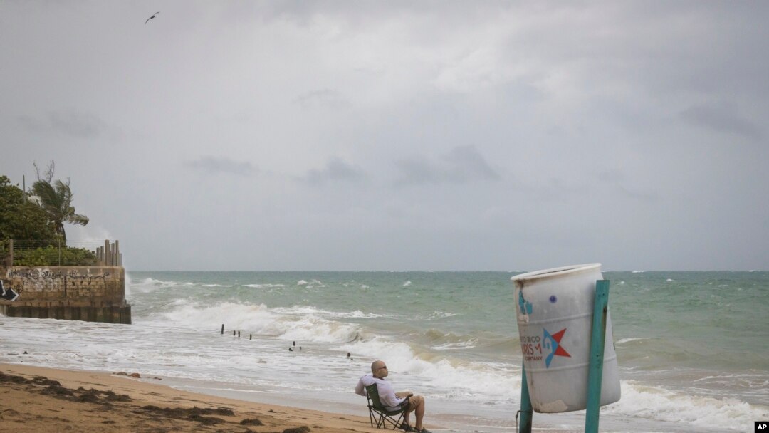 A man sits in front of a beach watching as the waves break before the arrival of Tropical Storm Fiona in San Juan, Puerto Rico, Sept. 17, 2022. 