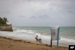 A man sits in front of a beach watching as the waves break before the arrival of Tropical Storm Fiona in San Juan, Puerto Rico, Sept. 17, 2022.