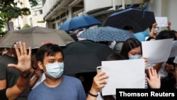 FILE - Supporters raise white paper to avoid slogans banned under the national security law as they support arrested anti-law protester outside Eastern court in Hong Kong, July 3, 2020.