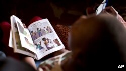 FILE - In this photo taken Feb. 16, 2015, a child holds a book while attending run by a Kenyan non-governmental organization in the Korogocho slum neighborhood of Nairobi, Kenya. an HIV-prevention session 