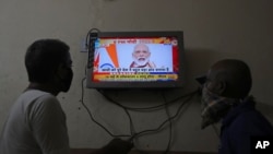Two people watch a televised address to the nation by Prime Minister Narendra Modi on economic stimulus measures, in Hyderabad, India, May 12, 2020.