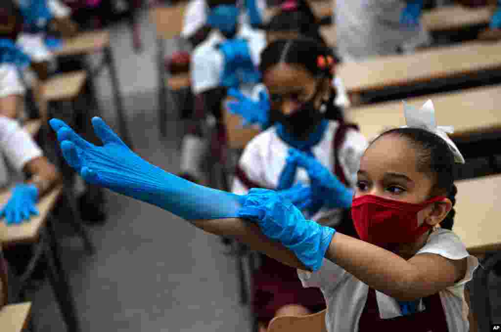 A student puts on plastic gloves as a precaution amid the spread of the new coronavirus during class in Havana, Cuba.